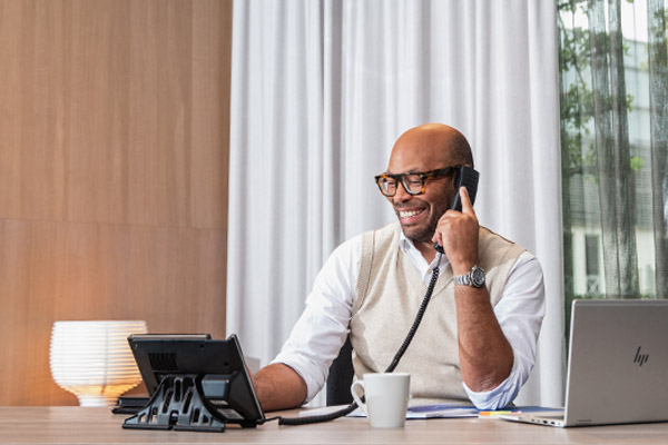 A man is sitting at a desk, smiling and talking on the phone.
