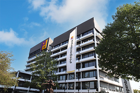 A large square building against a blue sky, with Piepenbrock flags.